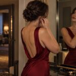 Femme élégante en robe rouge dos nu ajustant une boucle devant un miroir